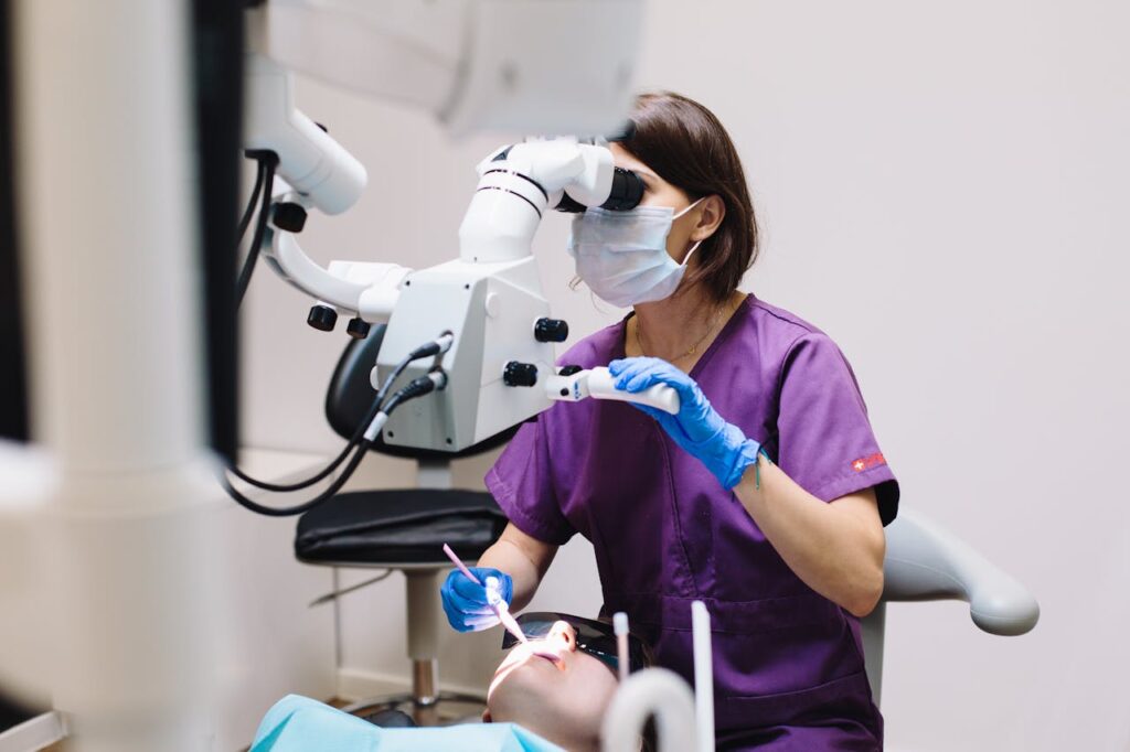 Woman in Purple Scrub Using a Dental Equipment in Examining a Patient